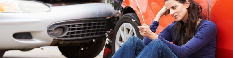 Letselschade na een botsing? Meld het bij ons Vrouw zit met telefoon in hand naast 2 gebotste auto's