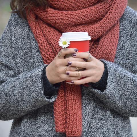 vrouw buiten met sjaal en koffie to go