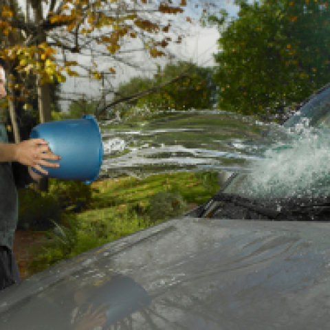 Wassen zonder vooraf afspoelen Man gooit emmer water over auto heen