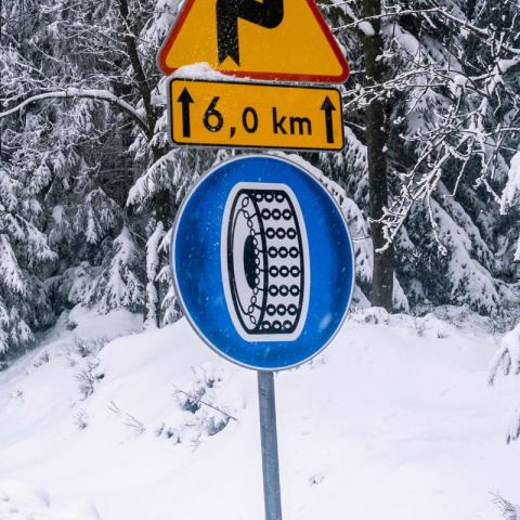 Verkeersbord dat het gebruik van sneeuwkettingen verplicht stelt langs een besneeuwde bosweg.