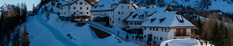 Monte Lussari bij Tarvisio: skiërs op een piste langs het bergdorp met het Santuario del Monte Lussari in de Italiaanse Alpen